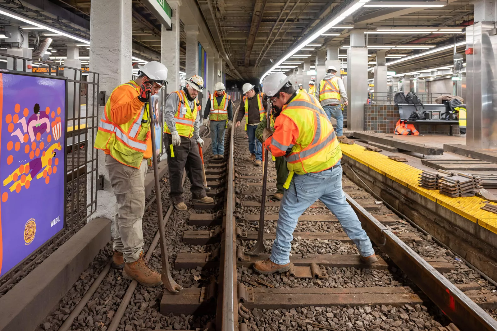 Track crew in hard hats and high-visibility vests replacing rail at a subway platform